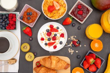 Kahvaltıda yanında tereyağlı kruvasan, mısır gevreği, fincanda süt, çilek, ahududu, kivi, kahvaltı masasında taze portakal suyu....