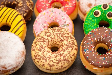 Tatlı, donut, çikolata ve çilek halkaları, şekerli ve kremalı çörekler ve sıcak kahve fincanları, ahşap masa arkasında kırılma veya parti hazırlığı.