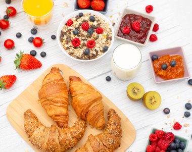 Kahvaltıda yanında tereyağlı kruvasan, mısır gevreği, fincanda süt, çilek, ahududu, kivi, kahvaltı masasında taze portakal suyu....