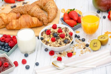 Kahvaltıda yanında tereyağlı kruvasan, mısır gevreği, fincanda süt, çilek, ahududu, kivi, kahvaltı masasında taze portakal suyu....