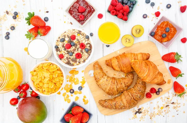 Kahvaltıda yanında tereyağlı kruvasan, mısır gevreği, fincanda süt, çilek, ahududu, kivi, kahvaltı masasında taze portakal suyu....