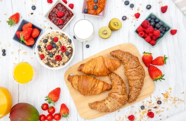 Kahvaltıda yanında tereyağlı kruvasan, mısır gevreği, fincanda süt, çilek, ahududu, kivi, kahvaltı masasında taze portakal suyu....