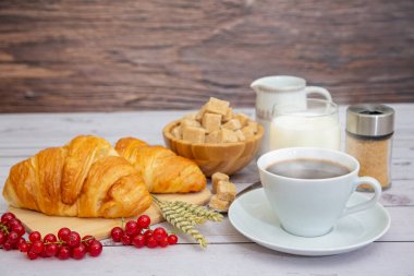 Sabah kahvaltısı, siyah kahve fincanı, ekmek, kruvasan ve ahşap masada meyve..
