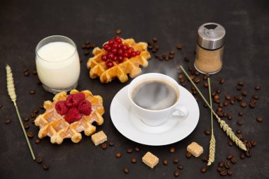 Sabah kahvaltıda siyah kahve fincanı, ekmek ve kruvasan ve siyah arka planda meyve..