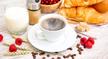 Sabah kahvaltısı, siyah kahve fincanı, ekmek, kruvasan ve ahşap masada meyve..