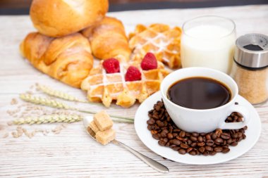 Sabah kahvaltısı, siyah kahve fincanı, ekmek, kruvasan ve ahşap masada meyve..