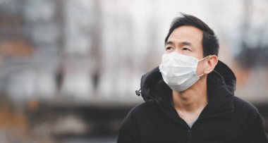 Mikropları, zehirli dumanları ve tozu önlemek için maske takan Asyalı genç bir adamın görüntüsü. Bakteriyel enfeksiyonun önlenmesi Corona virüsü veya Covid 19 sokaklarda ve bahçelerde.