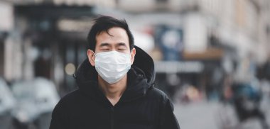 Mikropları, zehirli dumanları ve tozu önlemek için maske takan Asyalı genç bir adamın görüntüsü. Bakteriyel enfeksiyonun önlenmesi Corona virüsü veya Covid 19 sokaklarda ve bahçelerde.