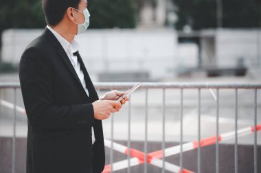 Mikropları, zehirli dumanları ve COVID 19 'u önlemek için doktor maskesi takan Asyalı bir adamın görüntüsü. Tablet ve gazetelerden haberleri okuyor ve dinliyor. Parkta çalışmıyor..