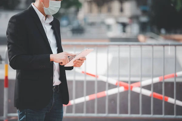 The image face of a Business Asian man wearing a doctor mask to prevent germs, toxic fumes, and COVID 19, He is reading and listening to the news on tablets and newspapers, do not work in the park.