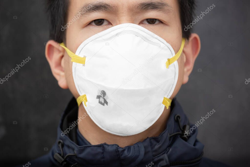 The face of Asian man wearing  N95 mask to prevent PM 2.5 dust and smog germs, toxic fumes, and dust, Prevention of bacterial infection Corona virus or Covid 19 on the black background.