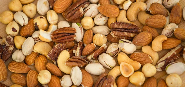 Hazelnut ,Pecan nut, Pistachio nut ,Peanuts nut,Almond nut mixed salt in a wooden plate is Protein food and healthy food for diet food on a black background.