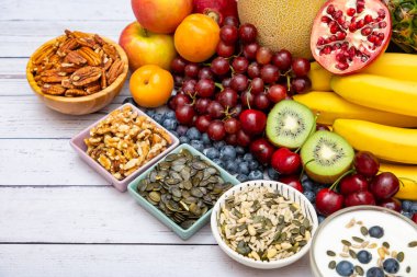 Grup fındıkları kuru, kaseye konur ve meyve muz, ananas ve üzüm tahta masa arkasında sağlıklıdır.