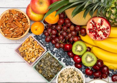 Grup fındıkları kaseye konur ve meyveler muz, ananas ve üzüm tahta masa arkasında sağlıklıdır.