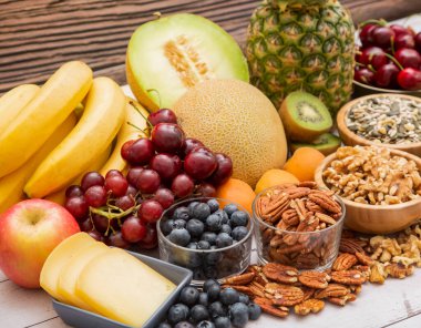 Grup fındıkları kaseye konur ve meyveler muz, ananas ve üzüm tahta masa arkasında sağlıklıdır.