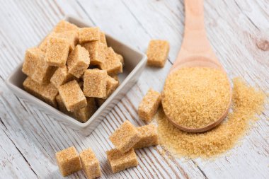 Kare bir fincanda esmer şeker ve ahşap bir masada tahta kaşık, sağlıklı şeker yemek veya tatlı pişirmek için kullanılır..