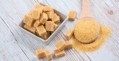 Kare bir fincanda esmer şeker ve ahşap bir masada tahta kaşık, sağlıklı şeker yemek veya tatlı pişirmek için kullanılır..