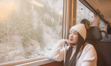 Asyalı bir kadın mutlu bir şekilde oturmuş trendeki doğal manzaraya bakıyor ve İsviçre 'ye tatile gidiyor ve tren yolculuğu planlıyor..