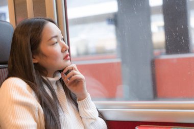 Asyalı bir kadın mutlu bir şekilde oturmuş trendeki doğal manzaraya bakıyor ve İsviçre 'ye tatile gidiyor ve tren yolculuğu planlıyor..
