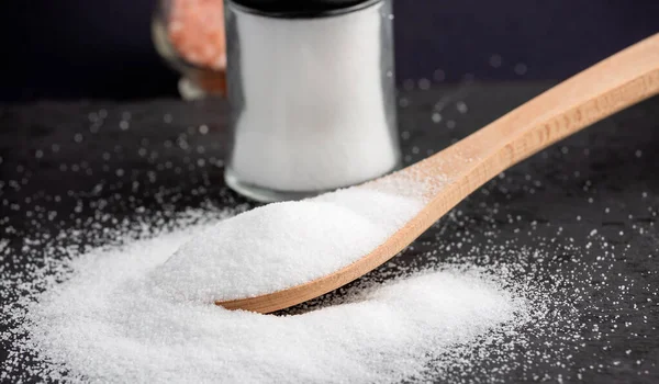 White sea salt for cooking food in Small glass bottles and wooden spoons on a stone tray background.