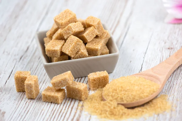 Brown sugar in a square cup and wooden spoon on a wooden table, healthy sugar is used for cooking food or desserts.