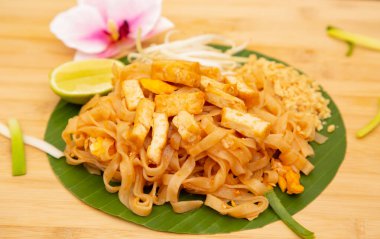 Pad Thai Tayland yemeği demirhindi sosu, fasulye lahanası ve taze soğanla karıştırılmış erişte ve tofu ahşap arka planda muz yaprağına konmuş beyaz yemektir.