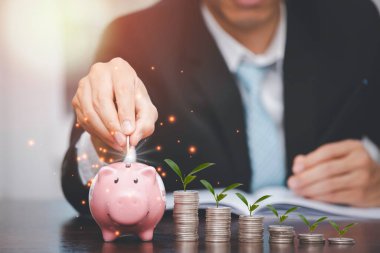 İşadamı, madeni paraların üzerine yaprak ve ahşap masanın üzerine domuzcuk koyarak fikirleri ve yatırım bütçesini, para tasarrufu kavramını, yer kopyalamayı kaydeden yaratıcı fikirleri topladı.