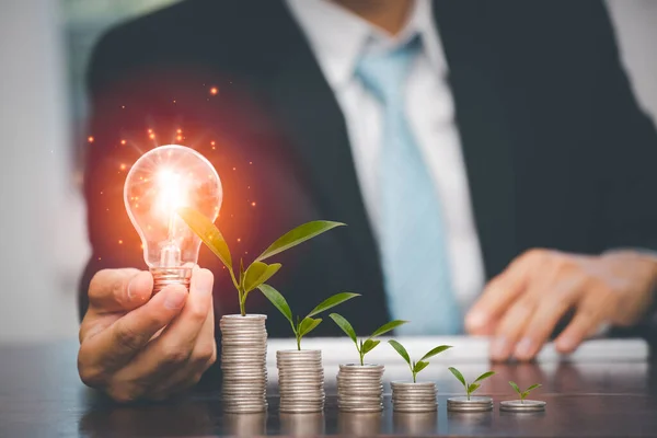 Businessman hand holding light bulb on coins stack on the wooden table , Saving ideas and investment budget, Creative ideas concept of saving money  concept, Copy space