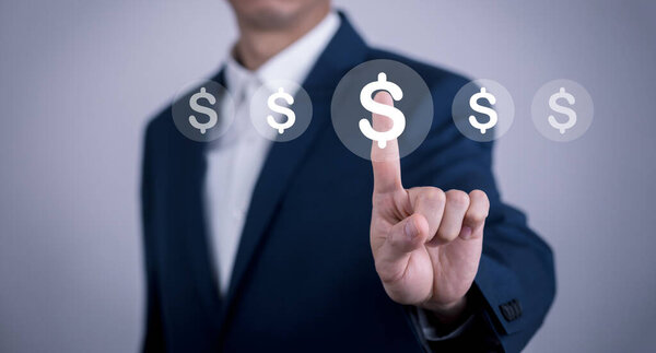 A businessman selects a virtual dollar sign icon, symbolizing financial decisions, investment, and digital transactions. The blurred background emphasizes modern technology and business strategy.
