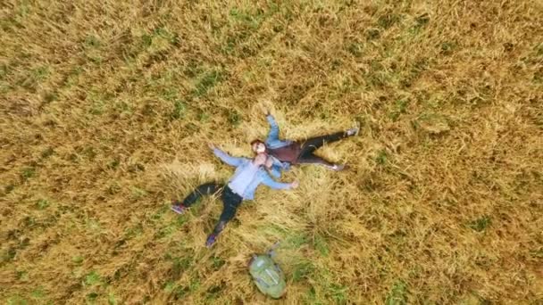 Un jeune homme et une jeune fille, voyageurs et auto-stoppeurs, se trouvent à côté d'un sac à dos sur un champ de céréales semé de blé ou de seigle . — Video