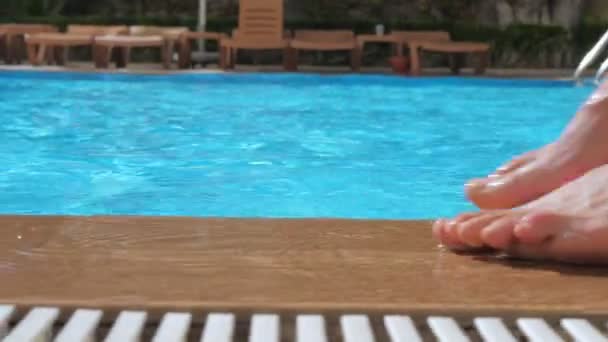 A girl with bare feet is walking along the edge of a pool of blue clear water. — Stock Video