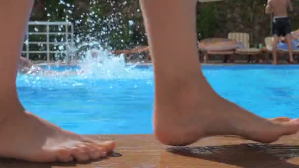Uma menina com os pés descalços está andando ao longo da borda de uma piscina de água clara azul . — Vídeo de Stock