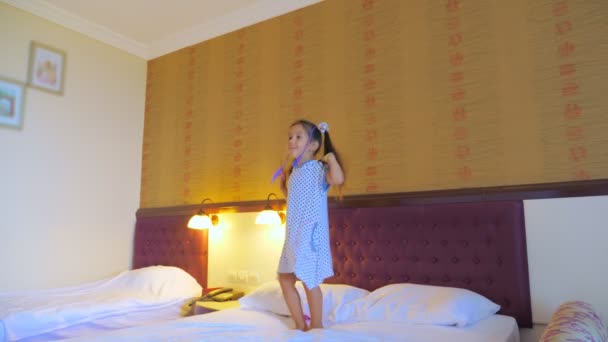 Uma menina salta na cama em um quarto de hotel, se diverte e gosta da vida . — Vídeo de Stock