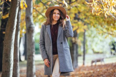 Açık havada rahat palto ve şapka sonbahar parkta yürüyen güzel genç kadın portresi. Sıcak güneşli havalarda. Güz konsepti.