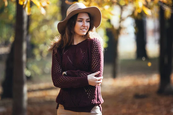 Porträt einer fröhlich lächelnden jungen Frau im herbstlichen Park in kuscheligem Pullover und Hut. warmes sonniges Wetter. Herbstkonzept. Kopierraum. — Stockfoto