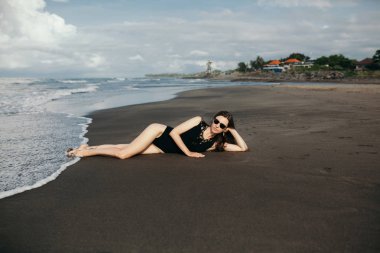 Güzel seksi kadın siyah mayo plajın kumları üzerinde rahatlatıcı. Güzel tan