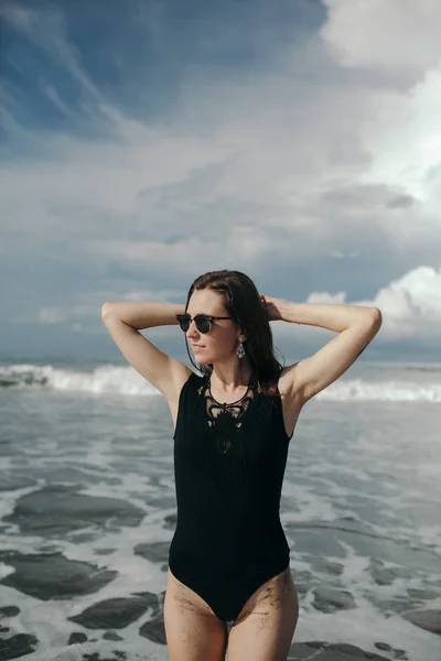 幸せな笑顔ブルネット身に着けている黒い水着の女性は黒砂のビーチの美しい空と海の背景で チャングー インドネシア バリ島 — ストック写真