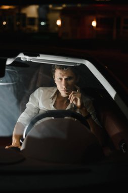Önden görünüm. Arabasını gece sürüş yakışıklı bir adam portresi. Trafik ışıkları arkasında.