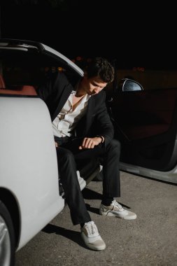 Beyaz cabriolet poz ve onun gözetiminde bakarak otururken yakışıklı bir adam portresi. Gece hayatı. Lüks araba takım elbiseli işadamı.