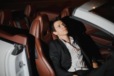 Şık genç adam oturma onun beyaz cabriolet poz açık portresi. Gece hayatı. Lüks araba takım elbiseli işadamı.