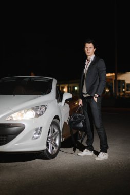 Onun beyaz cabriolet yanında ayakta şık genç adam. Gece hayatı. Lüks araba takım elbiseli işadamı.