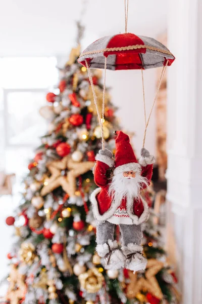 Santa Clause toy on parachute brings gifts at red Christmas tree bokeh background. Big Copyspace concept New Year banner, poster.