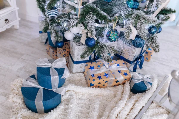 Regali di Natale avvolti in carta argento e blu, sfondo con luci di Natale bokeh di offuscata sotto l'albero di Natale. — Foto Stock