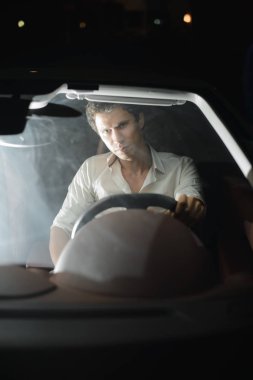 Genç bir adam yan görünümden kentsel bir sokakta onun araba kullanıyor. Gece, ya da kapalı otoparkta, aydınlatma