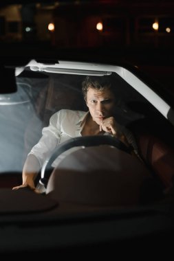 Yakışıklı moda adam araba cabriolet sürüş. Lüks. Gece hayatı. Trafik ışıkları arkasında.