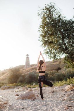 Ağaç poz karşı üzerinde kum plaj deniz feneri duran genç kadın silüeti