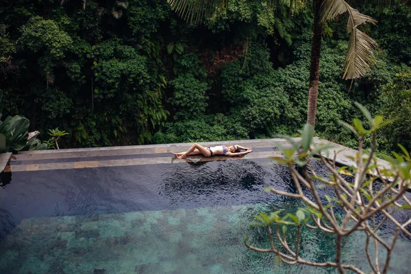 スリムなエッジ熱帯ジャングルの中でプールでリラックスした水着でセクシーなブルネットの女性 ヤシの木 クリスタルのきれいな水周り バリ島の高級リゾート — ストック写真