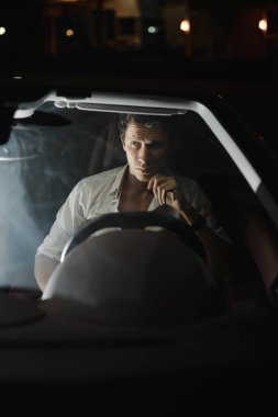 Önden görünüm. Arabasını gece sürüş yakışıklı bir adam portresi. Trafik ışıkları arkasında