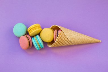 Dondurma waffle koni ile renkli macaron veya menekşe mor arka plan üstten görünüm üzerinde acıbadem kurabiyesi. Renkli şeker renkleri. Tatlı, tatlı, yaz konsepti. Üstten görünüm. Düz yatıyordu kompozisyon