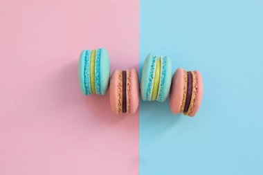Pembe ve mavi pastel arka plan, üstten görünüm üzerinde tatlı renkli Fransız acıbadem kurabiyesi kurabiye. Macarons yatıyordu yelpazesi paylamak.